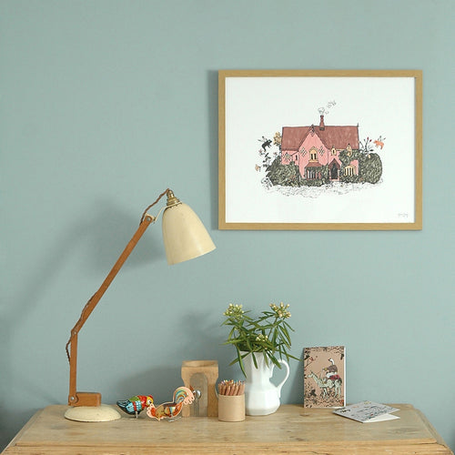 Framed print of a pink cottage illustration on a wall behind a desk