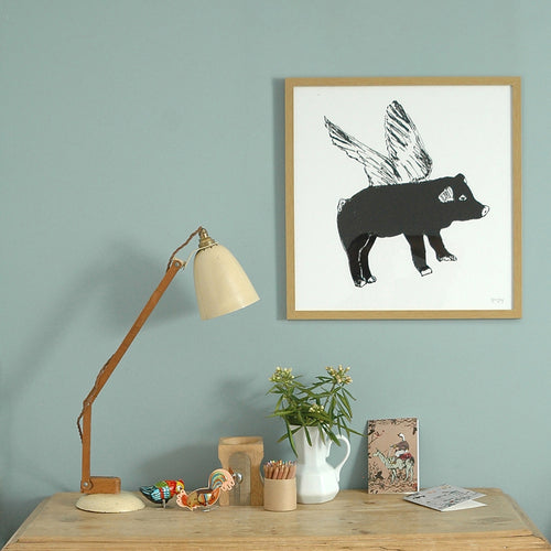 Framed print of a black flying pig illustration behind a desk