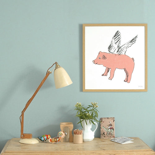 Framed print of a pink flying pig illustration on the wall behind a desk