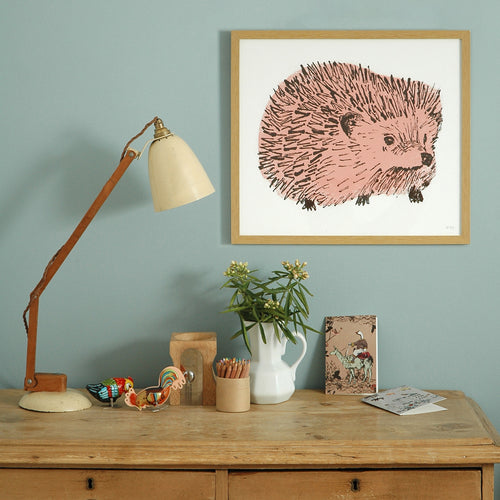 Framed print of a pink hedgehog illustration on wall behind a desk