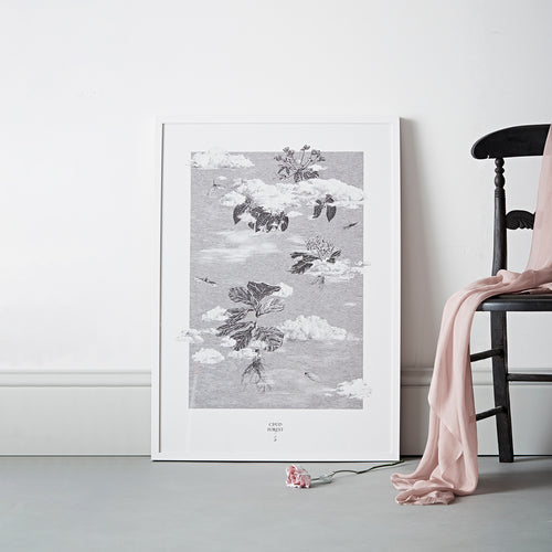 Framed print of seeds floating in between clouds illustration on floor next to chair